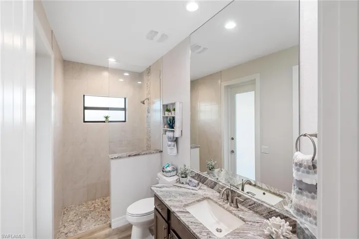 Bathroom with tiled shower, vanity, hardwood / wood-style flooring, and toilet
