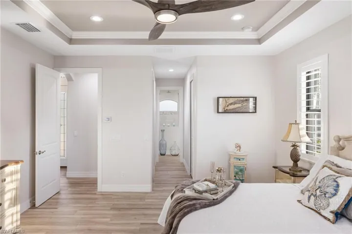 Bedroom with a raised ceiling, ceiling fan, light hardwood / wood-style floors, and ornamental molding