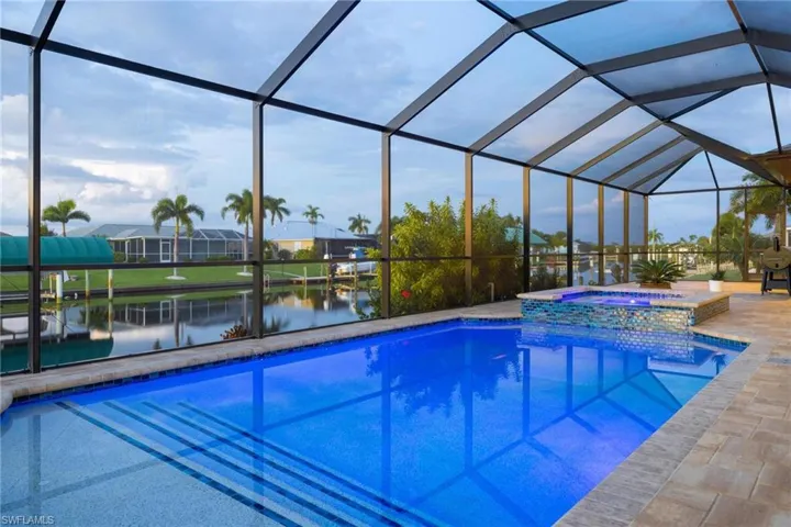 View of swimming pool with glass enclosure, an in ground hot tub, and a water view