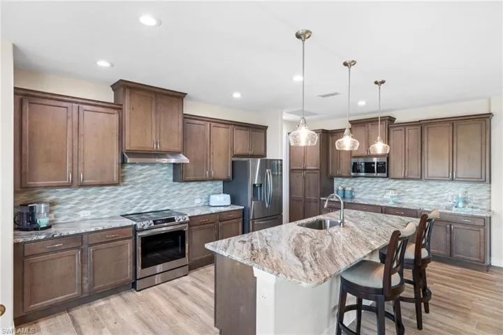Kitchen featuring sink, light wood-type flooring, appliances with stainless steel finishes, decorative light fixtures, and light stone counters