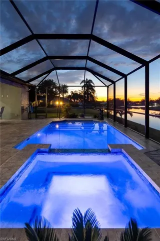 Pool at dusk featuring a lanai, a patio area, and a water view