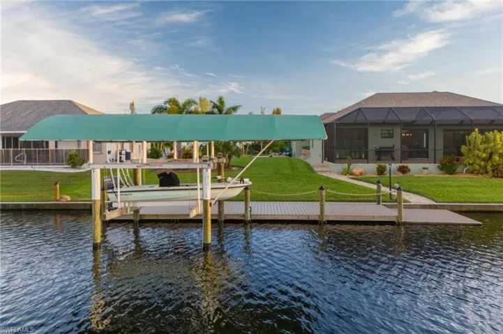 View of dock with a lanai, a water view, and a yard