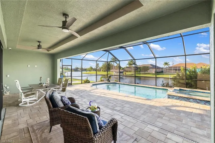 View of pool featuring ceiling fan, a lanai, an in ground hot tub, a water view, and a patio