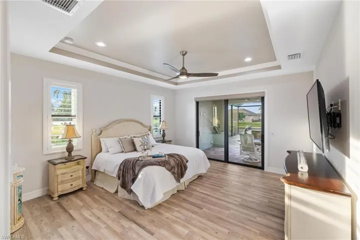 Bedroom with ceiling fan, light hardwood / wood-style flooring, access to outside, and a tray ceiling