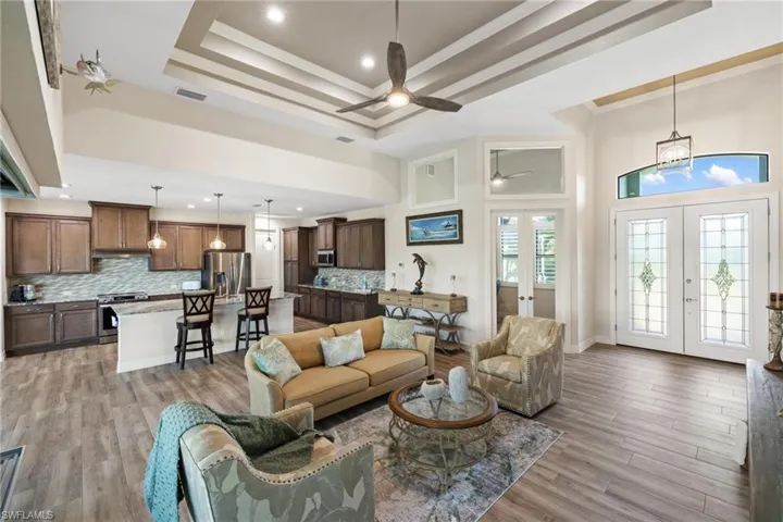 Living room featuring french doors, light wood-type flooring, a tray ceiling, ceiling fan, and a high ceiling