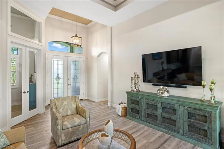 Living room featuring french doors, a towering ceiling, light hardwood / wood-style floors, and ornamental molding