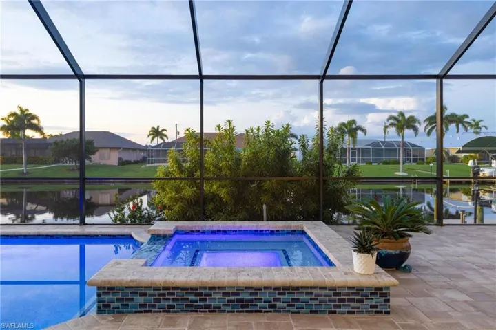 Pool at dusk featuring an in ground hot tub and glass enclosure