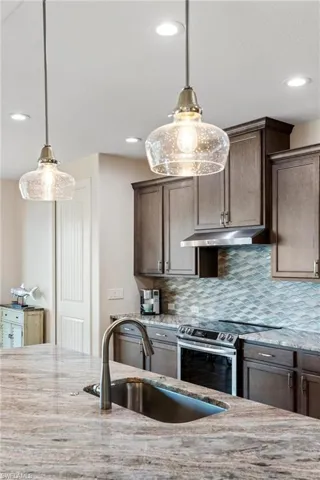 Kitchen with light stone counters, sink, stainless steel range with electric cooktop, and decorative light fixtures