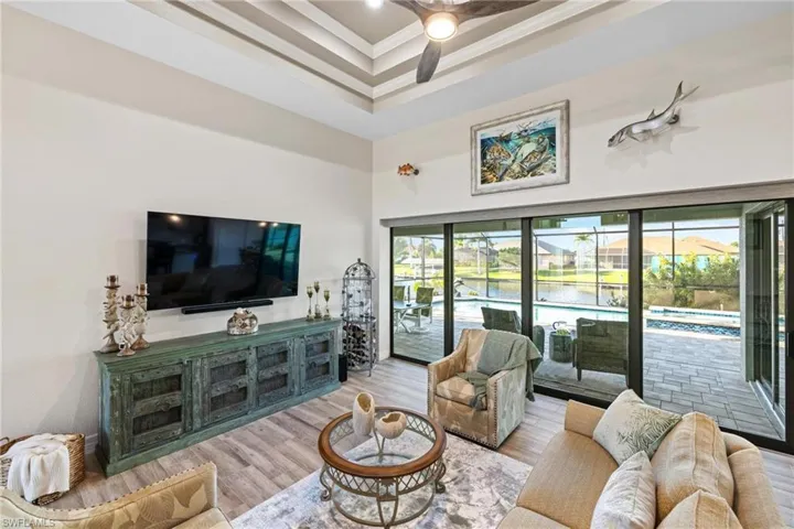 Living room featuring light wood-type flooring, a raised ceiling, ceiling fan, and crown molding