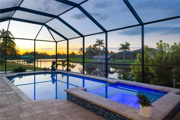 Pool at dusk with an in ground hot tub, a water view, and glass enclosure