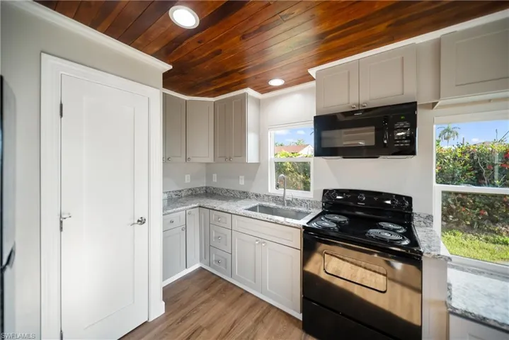 Kitchen with black appliances, a sink, wood ceiling, recessed lighting, and light wood-type flooring