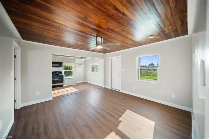 Unfurnished living room featuring a ceiling fan, wooden ceiling, baseboards, dark wood finished floors, and an AC wall unit