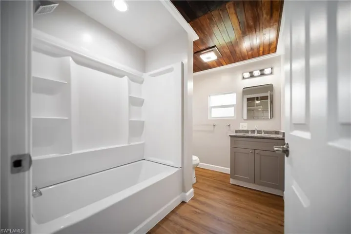 Bathroom with vanity, baseboards, toilet, shower / washtub combination, and wood ceiling