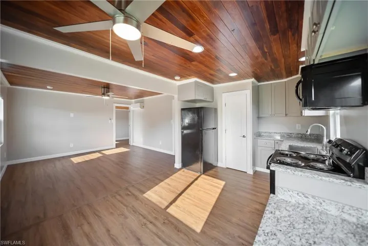 Kitchen with black appliances, wooden ceiling, ceiling fan, dark wood-type flooring, and a sink