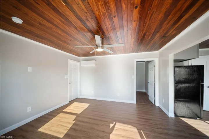 Living room featuring wooden ceiling, a wall unit AC, a ceiling fan, dark wood-style flooring, and baseboards