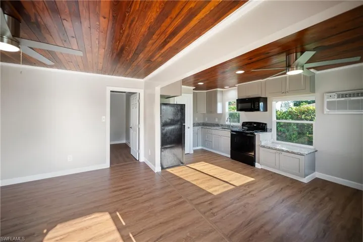 Kitchen featuring black appliances, a ceiling fan, a sink, wood ceiling, and an AC wall unit
