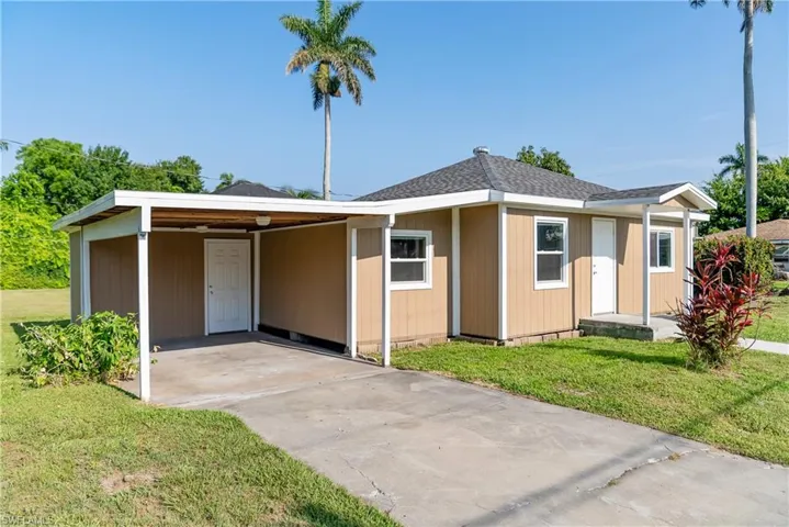 View of front of property featuring a front lawn, an attached carport, concrete driveway, and a shingled roof