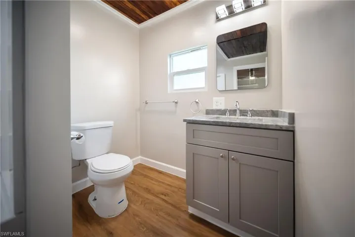 Full bath with toilet, vanity, baseboards, wood finished floors, and ornamental molding
