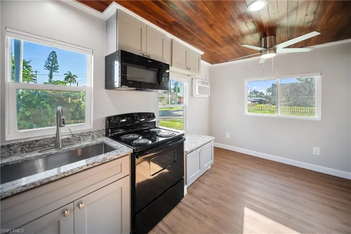 Kitchen with black appliances, a sink, wood ceiling, baseboards, and light stone countertops