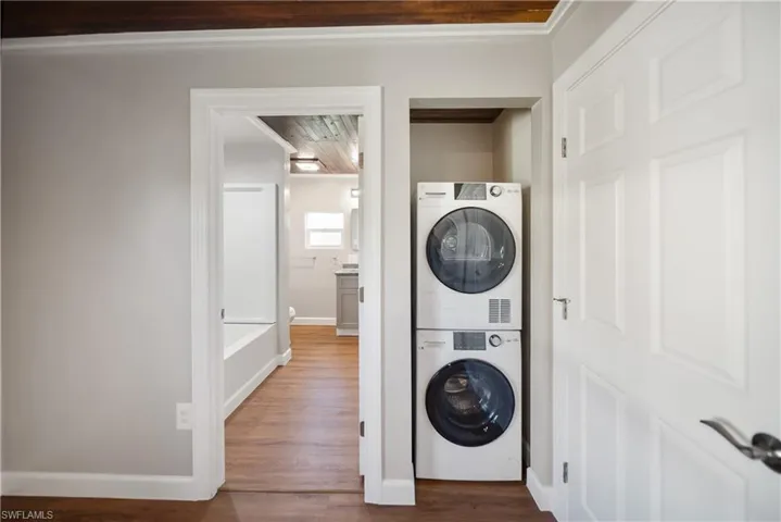 Laundry room with stacked washer and clothes dryer, dark wood-type flooring, and baseboards
