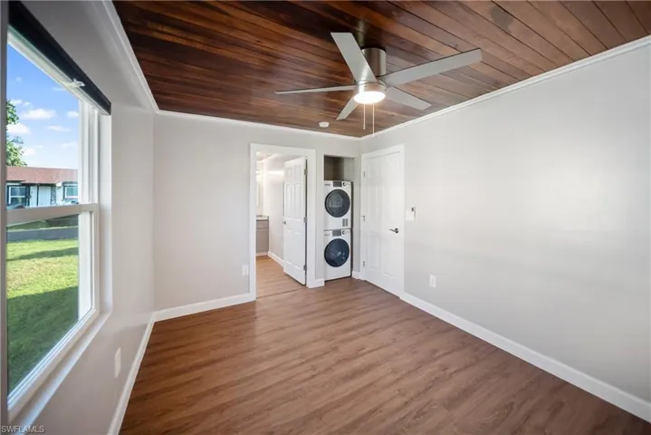 Spare room with estacked washer and dryer, wood ceiling, baseboards, a ceiling fan, and wood finished floors