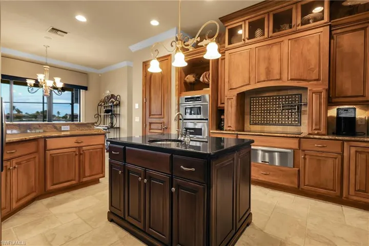 Kitchen with dark brown cabinetry, dark stone counters, crown molding, a chandelier, and a center island with sink