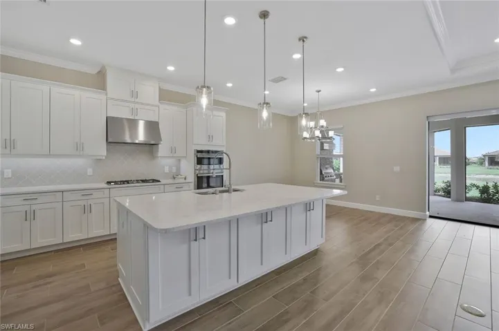 Kitchen with gas cooktop, under cabinet range hood, white cabinets, and light wood-type flooring