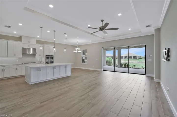 Kitchen with visible vents, baseboards, ceiling fan with notable chandelier, under cabinet range hood, and a raised ceiling