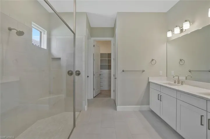Bathroom with tile patterned floors, a sink, a walk in closet, double vanity, and tiled shower