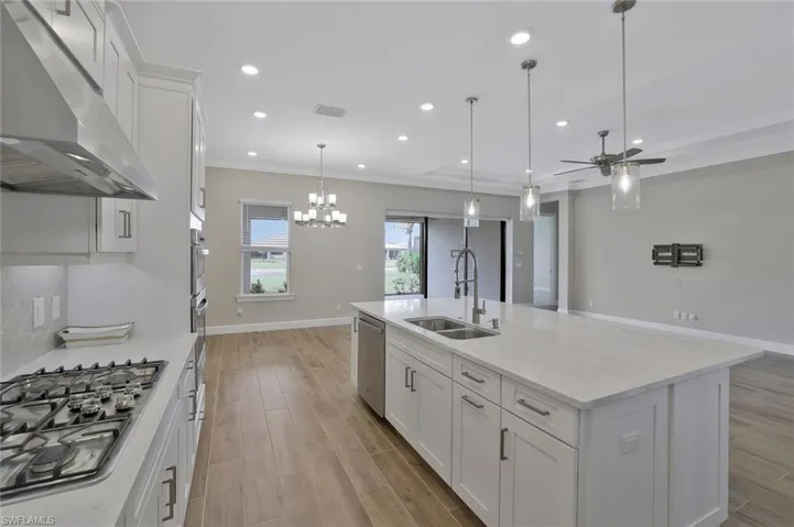 Kitchen featuring a sink, ceiling fan with notable chandelier, appliances with stainless steel finishes, white cabinets, and under cabinet range hood