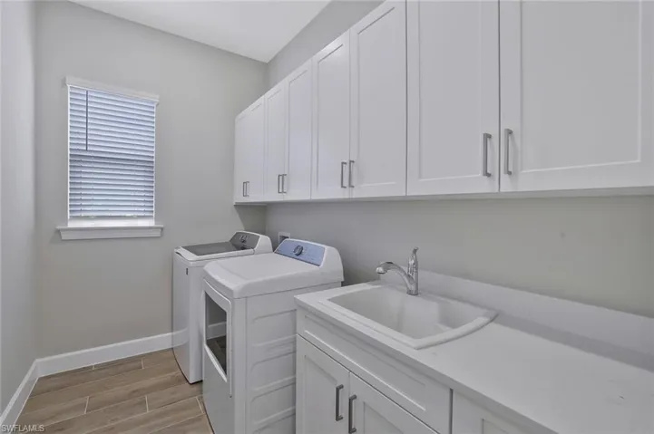 Laundry room featuring light wood finished floors, a sink, washing machine and dryer, baseboards, and cabinet space
