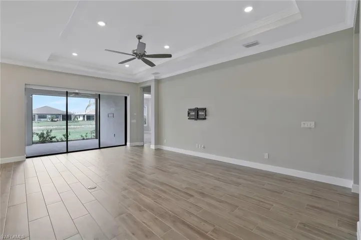 Spare room with light wood finished floors, a ceiling fan, a tray ceiling, and crown molding