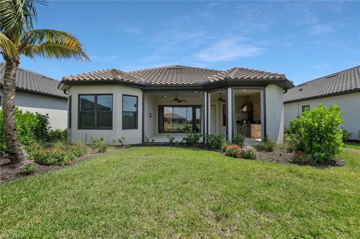Rear view of property featuring a tile roof, a ceiling fan, a yard, and stucco siding