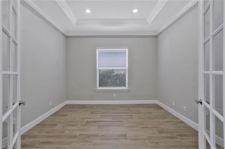 Spare room featuring a raised ceiling, french doors, crown molding, baseboards, and light wood-style flooring