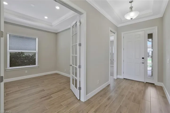 Entryway featuring a raised ceiling, light wood-type flooring, baseboards, and ornamental molding