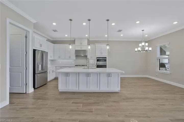 Kitchen featuring crown molding, stainless steel appliances, light countertops, under cabinet range hood, and visible vents
