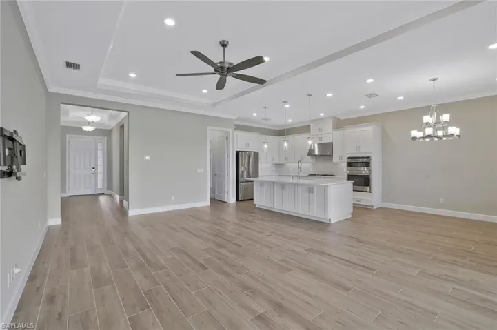 Unfurnished living room with a raised ceiling, visible vents, light wood-type flooring, baseboards, and ceiling fan with notable chandelier