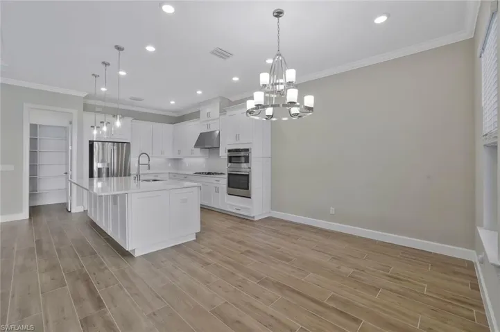 Kitchen with under cabinet range hood, light countertops, a sink, appliances with stainless steel finishes, and a notable chandelier