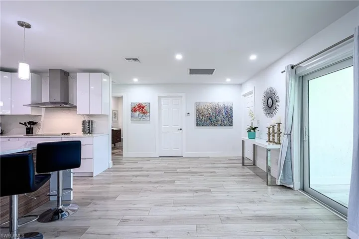 Kitchen featuring decorative light fixtures, decorative backsplash, white cabinetry, wall chimney range hood, and light wood-type flooring