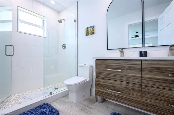 Bathroom featuring a shower with door, vanity, hardwood / wood-style floors, toilet, and ceiling fan