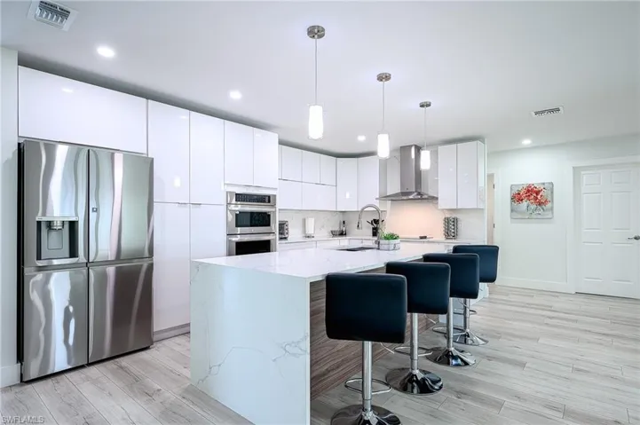 Kitchen with light hardwood / wood-style flooring, a center island, stainless steel appliances, wall chimney range hood, and white cabinets