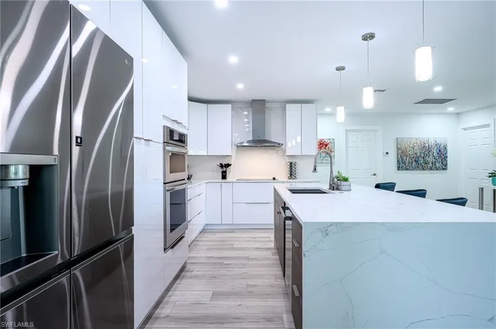 Kitchen featuring wall chimney range hood, appliances with stainless steel finishes, white cabinetry, and decorative light fixtures