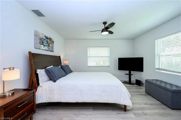 Bedroom with ceiling fan, light wood-type flooring, and multiple windows
