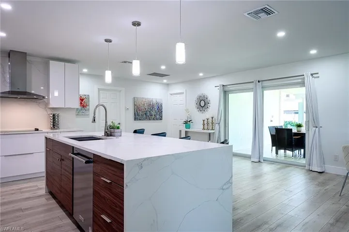 Kitchen featuring light wood-type flooring, white cabinetry, an island with sink, wall chimney exhaust hood, and pendant lighting