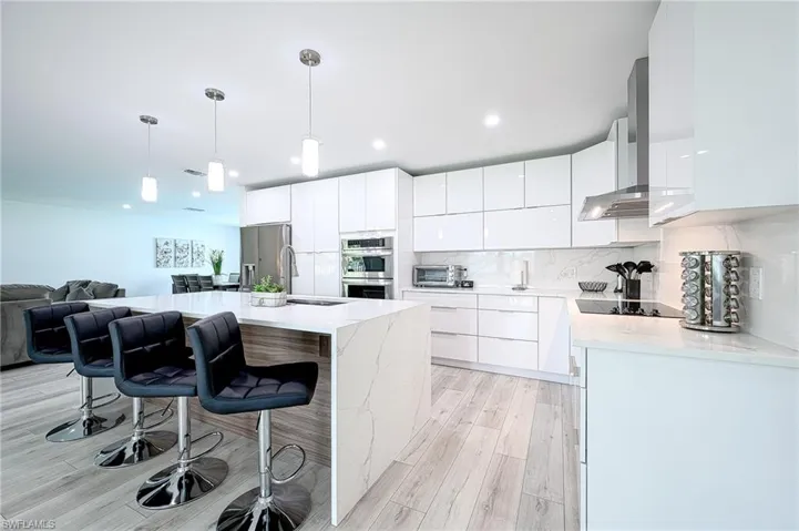Kitchen with white cabinets, light hardwood / wood-style flooring, stainless steel appliances, pendant lighting, and a center island with sink