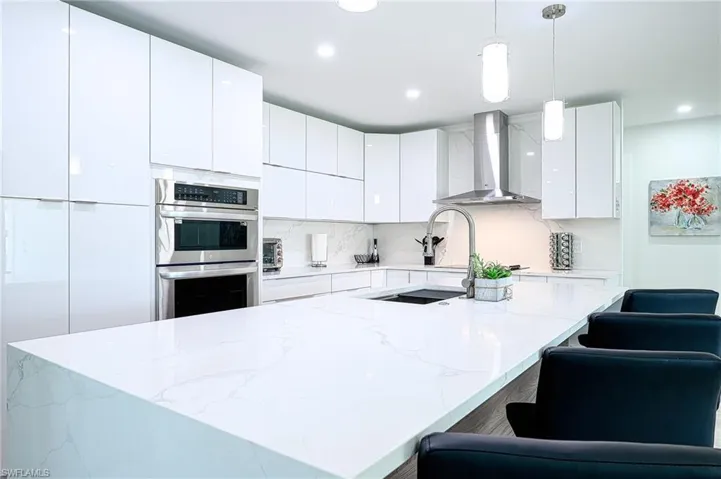 Kitchen with hanging light fixtures, a center island, wall chimney range hood, and white cabinetry