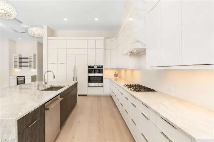 Kitchen with modern cabinets, light stone countertops, white cabinetry, stainless steel appliances, and light wood finished floors