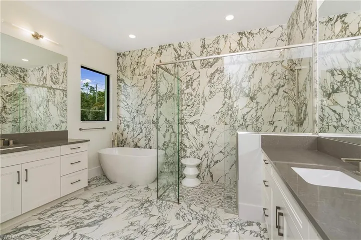 Bathroom featuring tile walls, two vanities, stone wall, a freestanding tub, and a marble finish shower