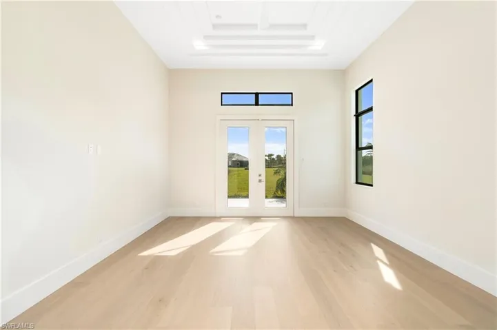 Unfurnished room with light wood finished floors, a tray ceiling, french doors, and a towering ceiling