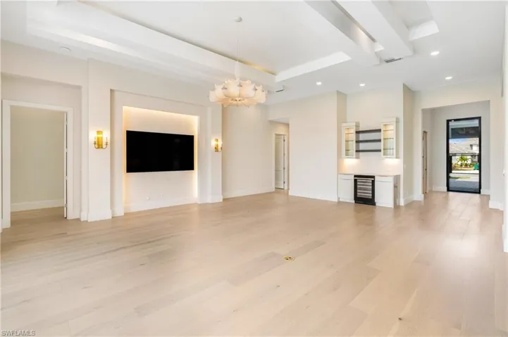 Unfurnished living room featuring a chandelier, recessed lighting, light wood-type flooring, wine cooler, and a raised ceiling